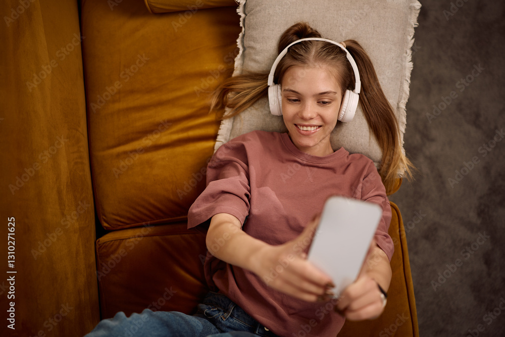 Above view of happy teenager taking selfie with her cell phone at home. Above view of happy teenager taking selfie with her cell phone at home.