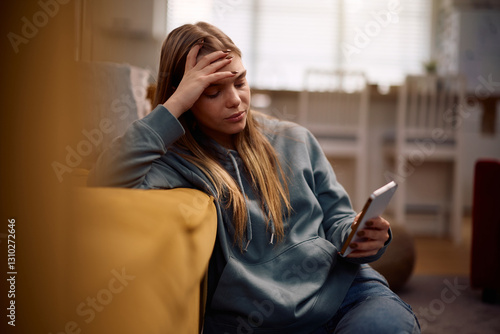 Canvas Print Sad teenage girl reading text message on mobile phone at home.