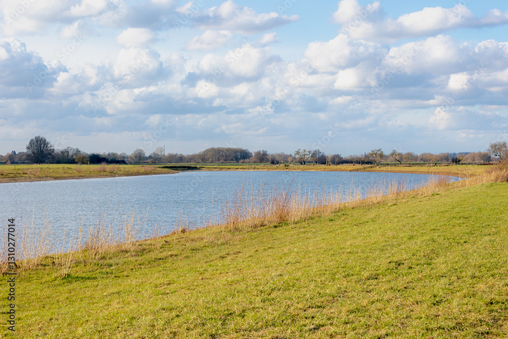 Landscape view of the river under blue sky, The IJssel is a Dutch distributary of the river Rhine that flows northward and ultimately discharges into the IJsselmeer, Deventer, Overijssel, Netherlands. Landscape view of the river under blue sky, The IJssel is a Dutch distributary of the river Rhine that flows northward and ultimately discharges into the IJsselmeer, Deventer, Overijssel, Netherlands.