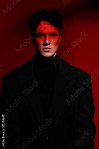 Close Up portrait of a handsome serious young man in black suit over red dark background. Horizontal view. Space for text.
