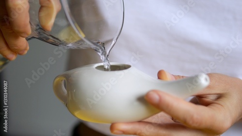 Healthcare professional pouring sterile water into ceramic neti pot, performing nasal irrigation technique targeting sinus congestion and respiratory wellness. concept of nasopharynx cavity hygiene photo