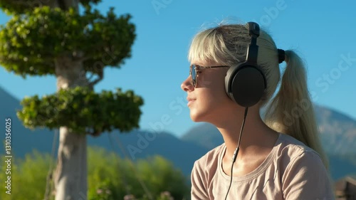 Wallpaper Mural Millennial teen in earphones in nature. A cute millennial young girl relax in headphones on green bay in sun light. Torontodigital.ca