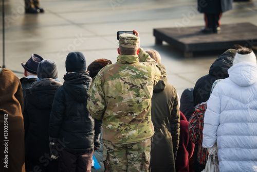 An American soldier in uniform takes a picture on his phone in the crowd at a military parade in Tallinn. photo