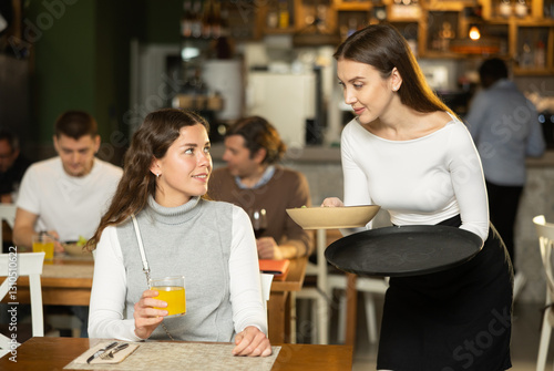 Female waitress brings freshly cooked food to a client against the background of other visitors to the restaurant. European woman gets quality food and service in a restaurant