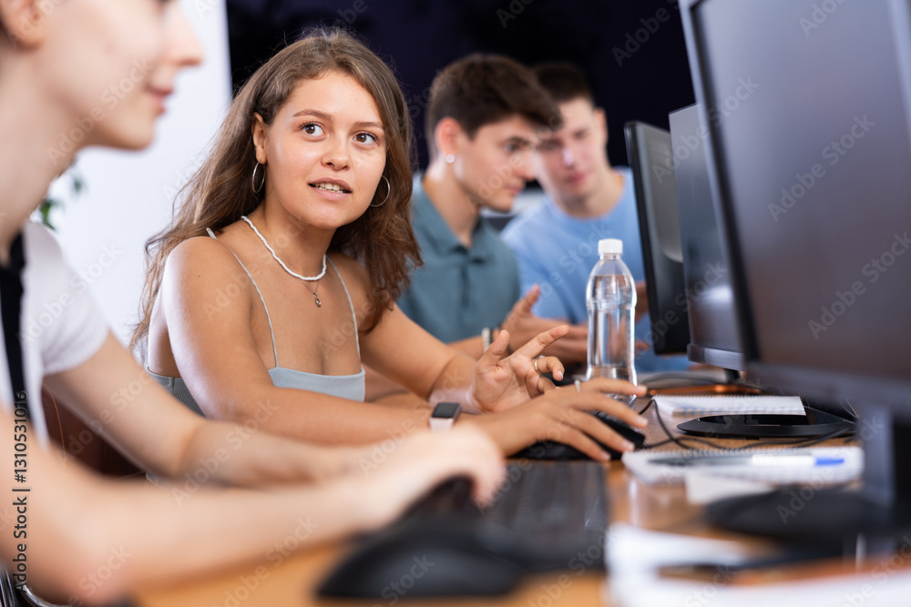 Fototapeta premium Portrait of interested motivated young female software developer working in IT startup, sitting at computer desk and coding with group of coworkers