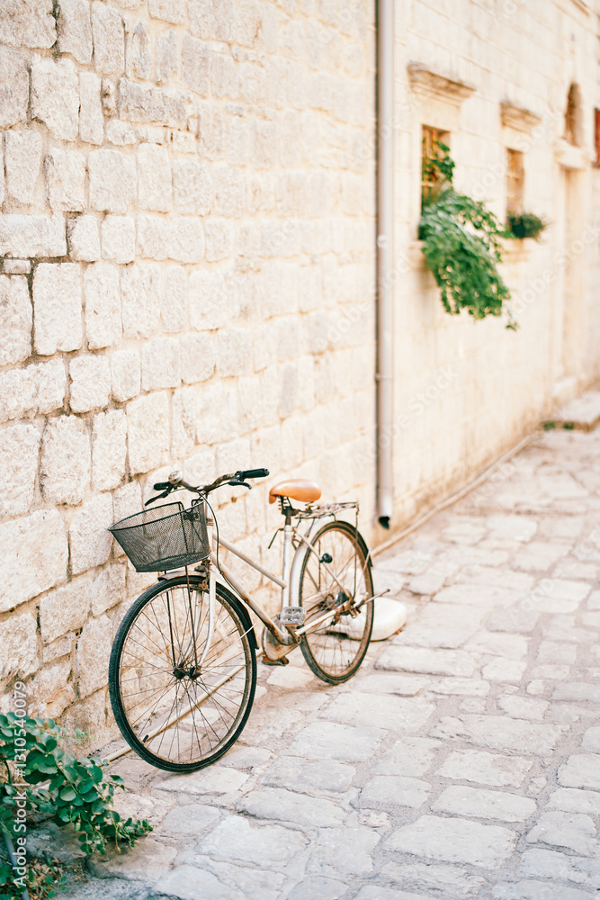 Lady bicycle with a basket on the handlebars stands near the stone wall of an old house Lady bicycle with a basket on the handlebars stands near the stone wall of an old house