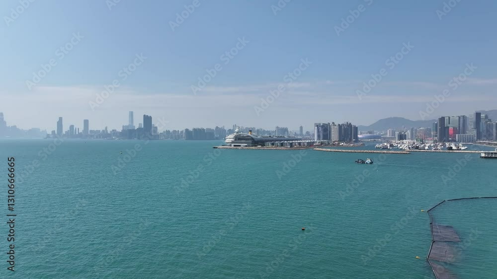 Drone aerial skyview of a mega luxury cruise ship sailing at the Kai Tak cruise terminal, showcasing the vibrant Victoria Harbour and the iconic city skyline of Kwun Tong Kowloon Hong Kong Drone aerial skyview of a mega luxury cruise ship sailing at the Kai Tak cruise terminal, showcasing the vibrant Victoria Harbour and the iconic city skyline of Kwun Tong Kowloon Hong Kong