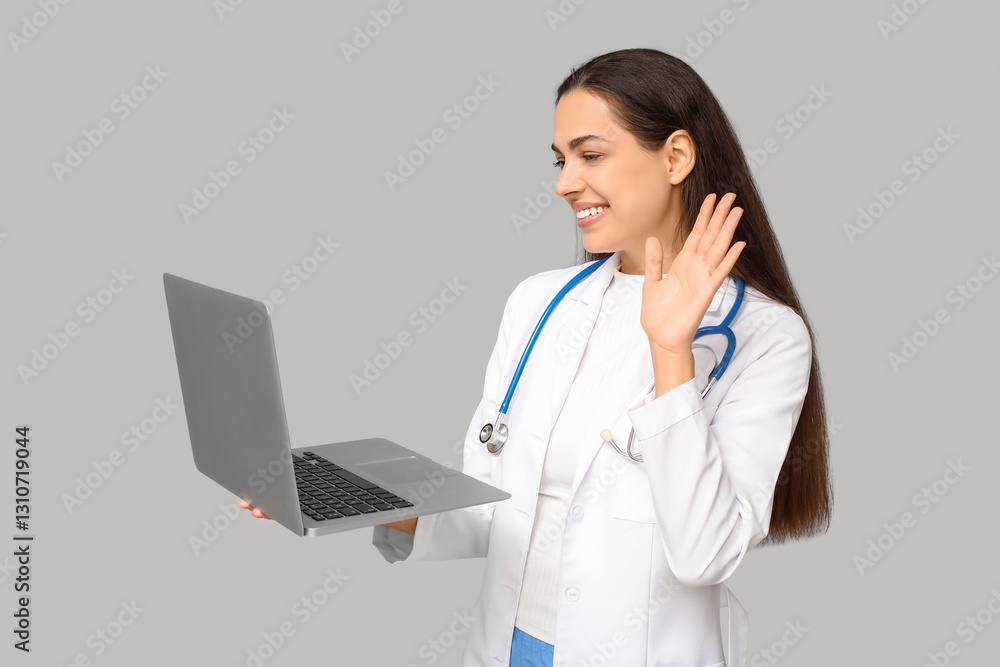 Portrait of female doctor with modern laptop waving hand on grey background Portrait of female doctor with modern laptop waving hand on grey background
