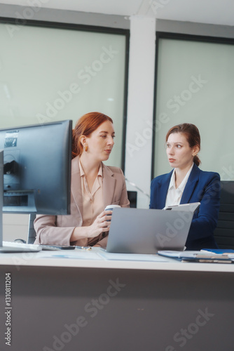 Obraz na płótnie Two Caucasian women work in an office, happily using laptops and computers at a desk, discussing financial projects, analyzing financial statements,collaborating in a meeting to ensure effective w salonie