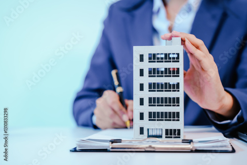 A female employee works at her desk in a real estate office, managing condo sales in the city. She communicates with clients, handles listings, and provides information about available properties