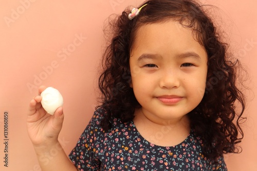 Portrait of an Asian female toddler eating boiled eggs on a pink background, close up.