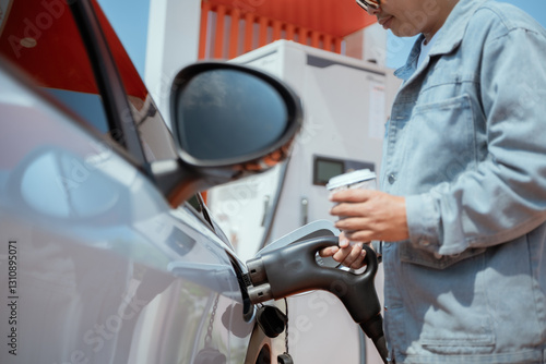 Man refuels car while holding a beverage at a modern gas station in bright daylight