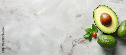Freshly cut avocado showcasing a vibrant green flesh on a elegant marble background with dark green whole avocados and small red berry in bottom left corner.
