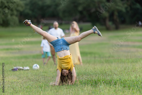 Konstfotografi Young girl doing a cartwheel in the park while family watches