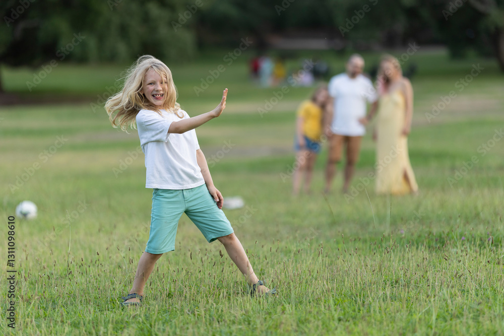 Blond boy playing in the park with family watching in background Blond boy playing in the park with family watching in background
