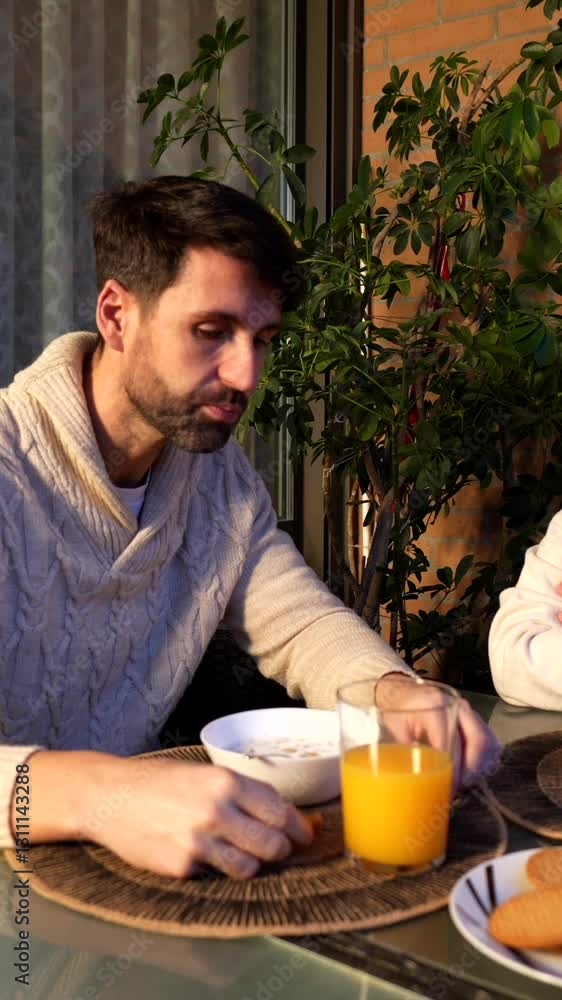 Romantic couple having breakfast together on their balcony, talking and eating cookies and orange juice Romantic couple having breakfast together on their balcony, talking and eating cookies and orange juice