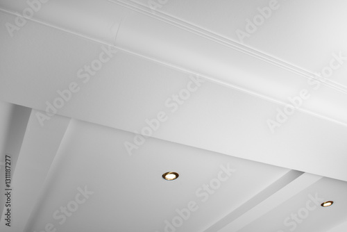 Suspended and grid ceiling with LED spots lamps and drywall construction in empty room in house interior. Stretch ceiling white and complex shape.