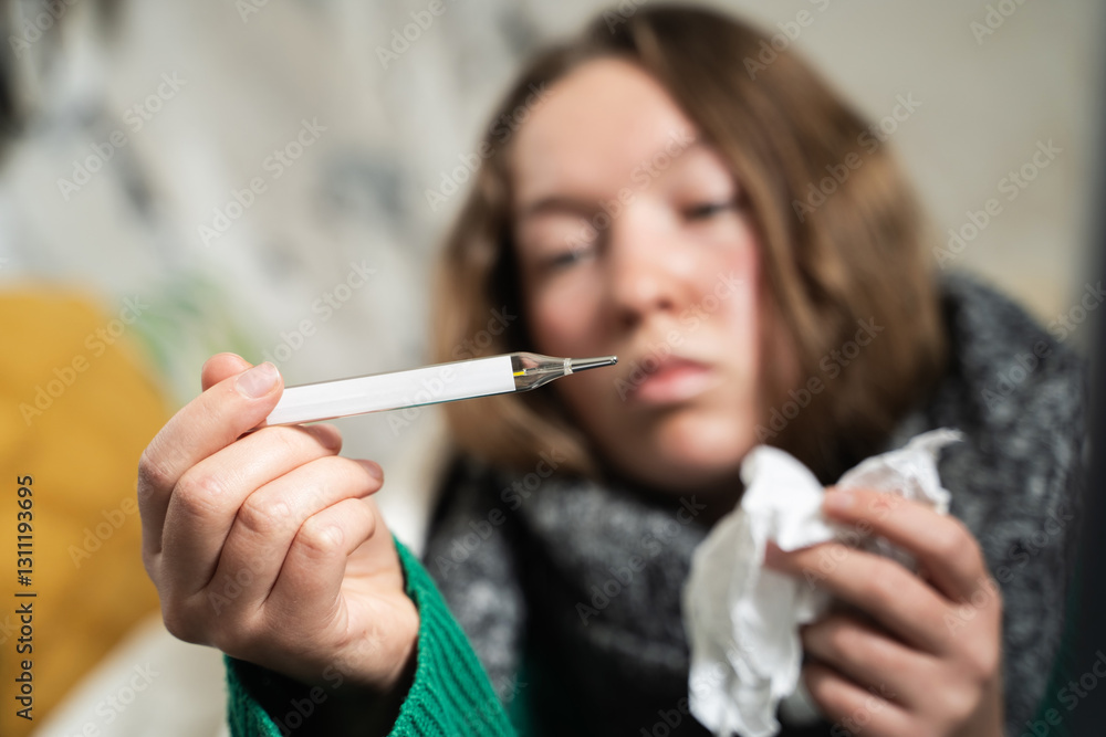 Young sick woman with high fever checking thermometer during illness, lying in bed, looking exhausted and tired. Girl measures the temperature. Influenza, seasonal flu, cold. Home treatment. Young sick woman with high fever checking thermometer during illness, lying in bed, looking exhausted and tired. Girl measures the temperature. Influenza, seasonal flu, cold. Home treatment.