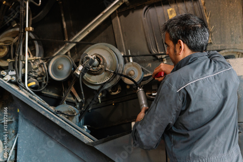 Farmer performing maintenance on agricultural machinery using grease gun