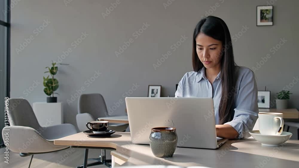 A freelancer working on a laptop in a minimalistic home office with a cup of coffee next to them. A freelancer working on a laptop in a minimalistic home office with a cup of coffee next to them.