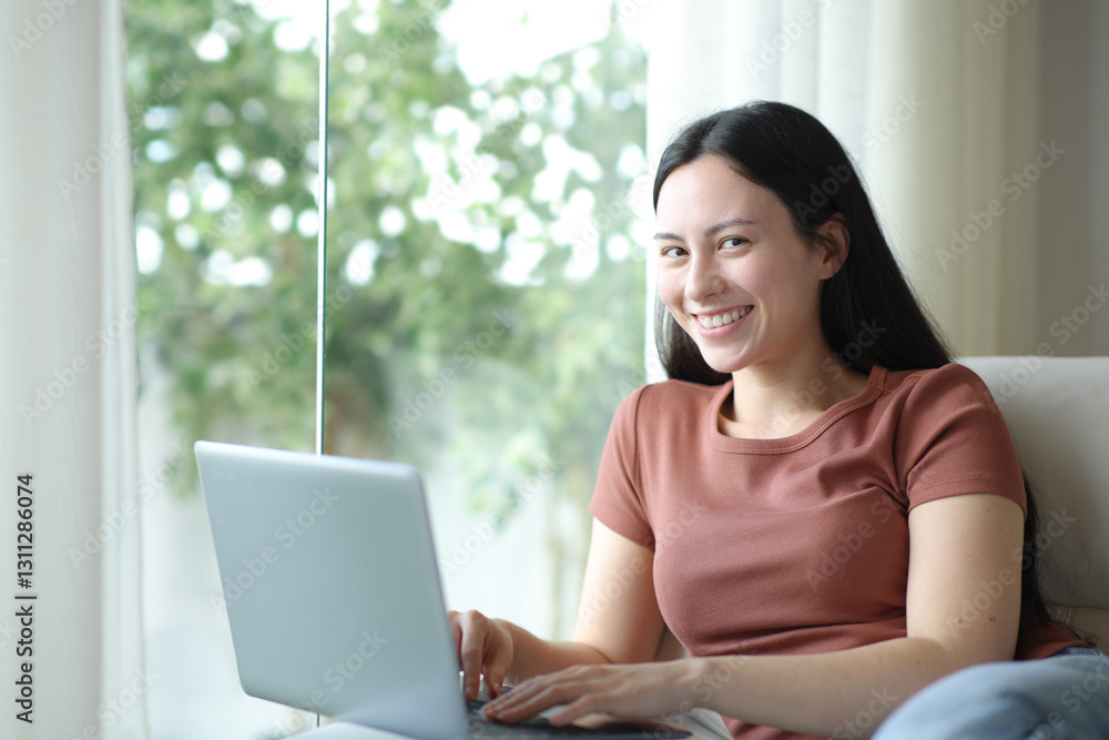 Happy asian woman using laptop looking at camera in a house Happy asian woman using laptop looking at camera in a house