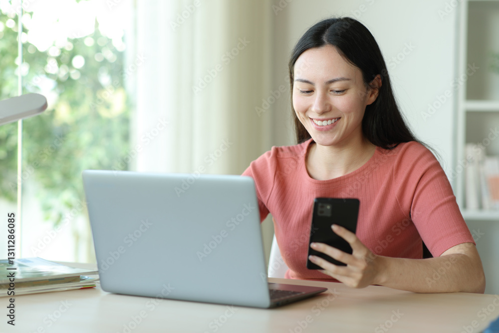 Happy asian woman using phone and laptop in a desk