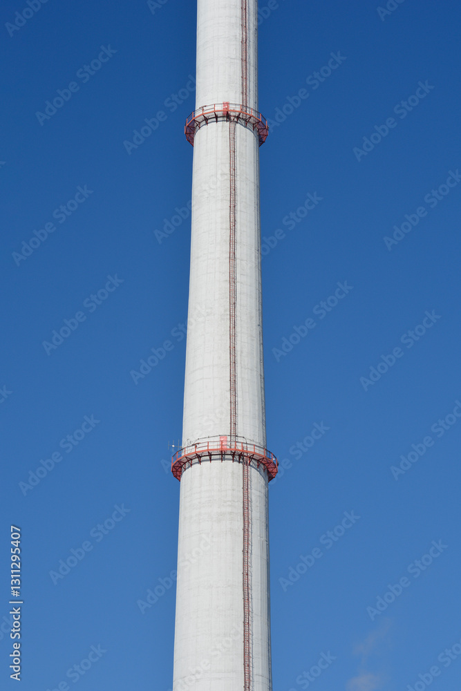 A tall concrete chimney with two red maintenance platforms, rising against a clear blue sky A tall concrete chimney with two red maintenance platforms, rising against a clear blue sky