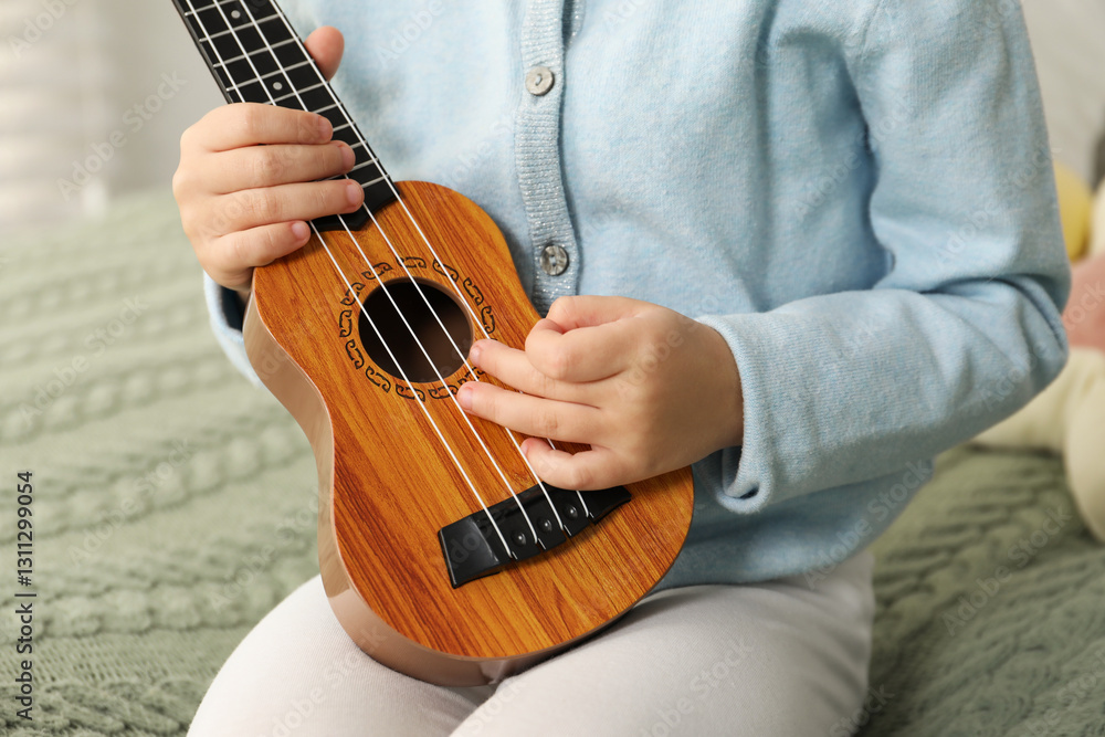 Fototapeta premium Little girl with ukulele on bed at home, closeup