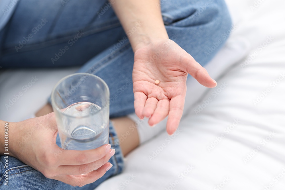 Fototapeta premium Woman with contraceptive pill and glass of water on bed, closeup