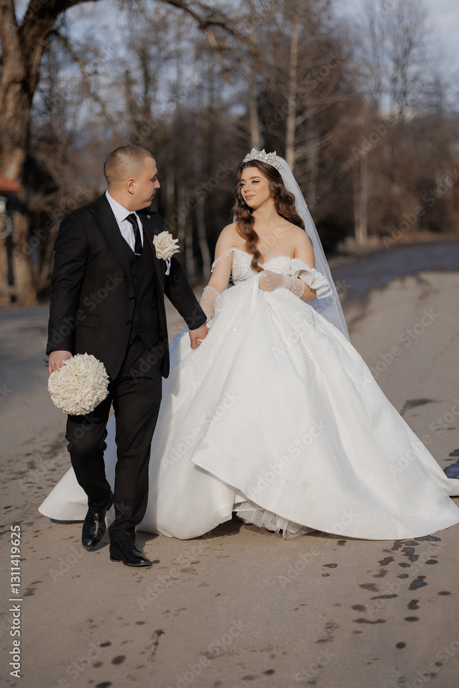 A bride and groom are walking down a road in a wedding dress and suit. The bride is wearing a tiara and the groom is holding a bouquet A bride and groom are walking down a road in a wedding dress and suit. The bride is wearing a tiara and the groom is holding a bouquet