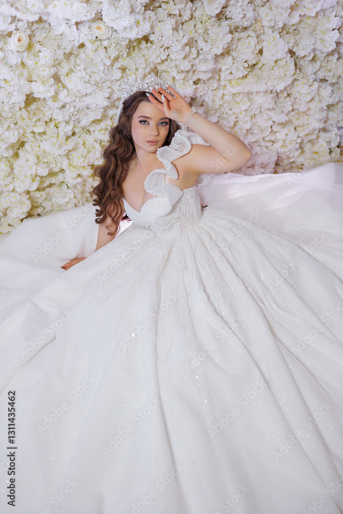 Fototapeta premium A woman is wearing a white dress with a tiara on her head. She is sitting on a bed and looking at the camera. The dress is long and has a lot of sparkles, giving it a glamorous and elegant appearance