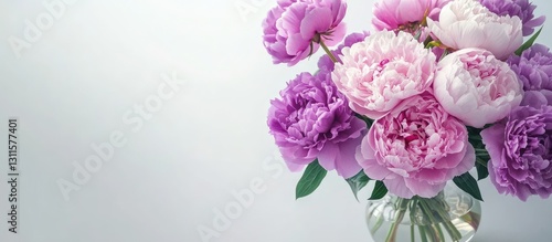 Obraz na płótnie Elegant arrangement of pink and purple peonies in a clear vase on a white table with soft light; space for text on the right side. w salonie