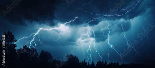Dramatic nighttime thunderstorm showcasing bright blue lightning bolts striking from dark storm clouds above silhouetted trees in the foreground