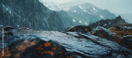 Obraz na płótnie Moody wet mountainside with dark rocky foreground and blurred distant peaks under gray sky capturing rain droplets and vibrant rock textures. w salonie