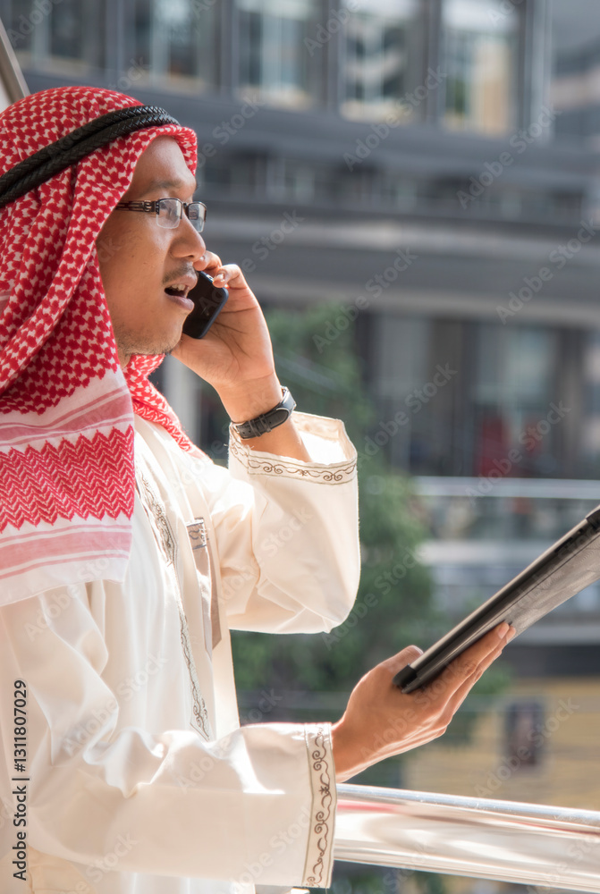 Fototapeta premium Portrait Vertical Islamic man smile look at camera wear muslim dress in modern uae city. Vertical horizon Arab men wear hijab Headscarf muslim formal dress lifestyle. Arabman saudi Arabian Culture