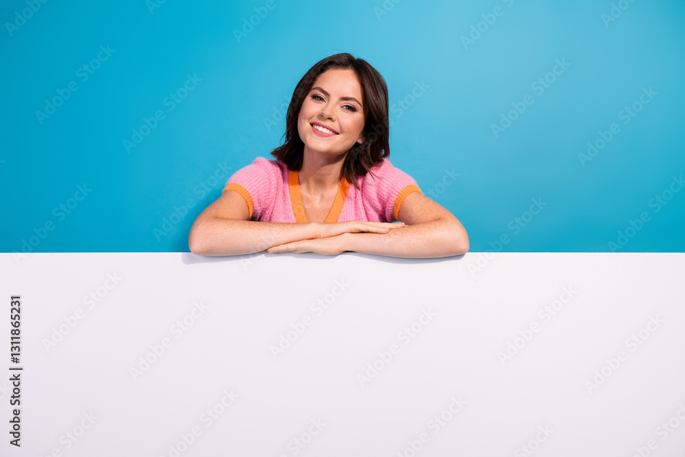 Smiling young woman leaning on a white board against a blue background in a casual pink top Smiling young woman leaning on a white board against a blue background in a casual pink top