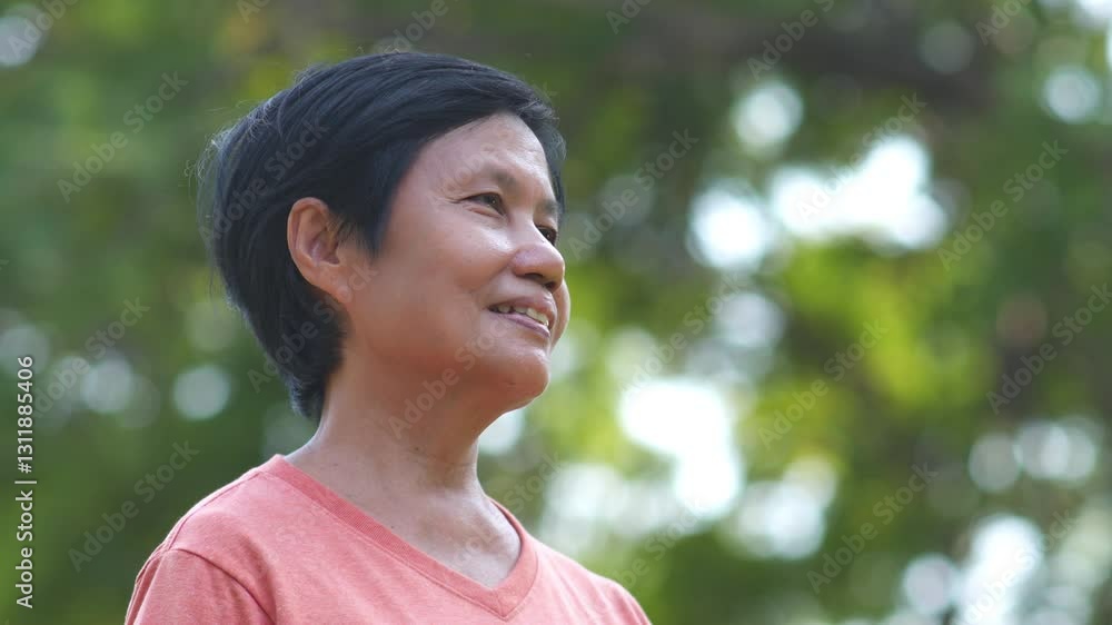 Smiling Senior Asian woman standing outdoors with a blurred green foliage background. Smiling Senior Asian woman standing outdoors with a blurred green foliage background.