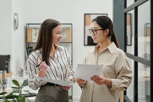 Tablou pe pânză Side view portrait of two smiling young businesswomen looking at each other whil