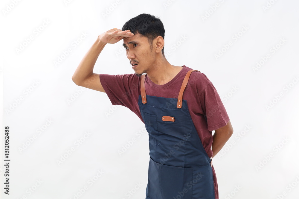 Portrait of curious asian man in apron holding hand above eyes and peering into distance, looking far away, expecting and searching someone. studio shot isolated Portrait of curious asian man in apron holding hand above eyes and peering into distance, looking far away, expecting and searching someone. studio shot isolated