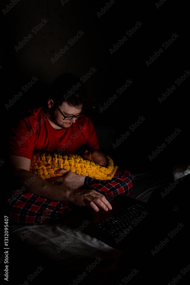 Father Holding Baby While Using Laptop in Dim Light