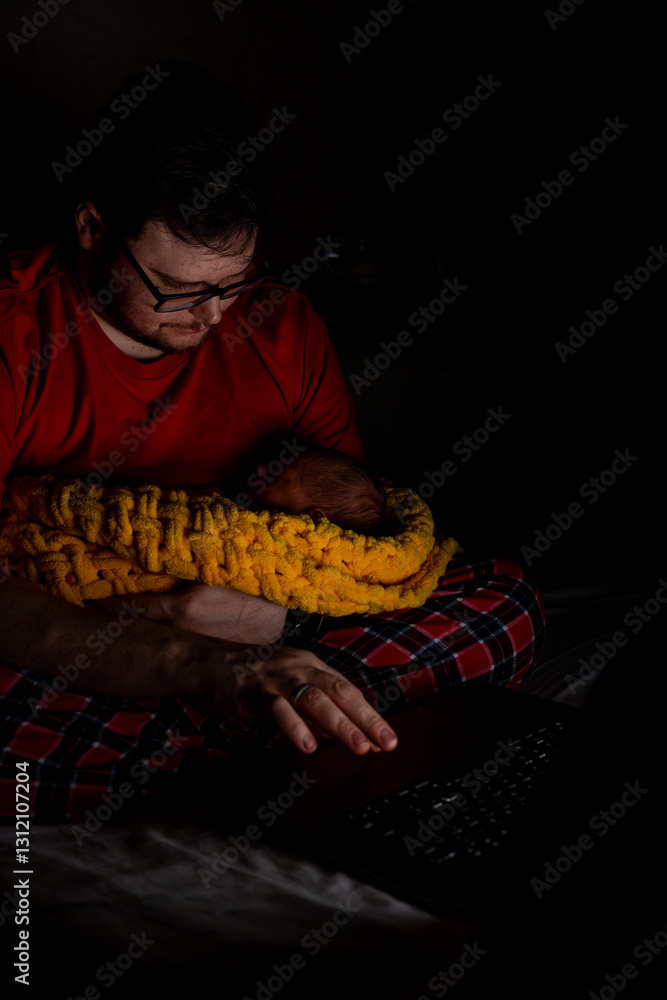 Father Holding Baby While Using Laptop in Dim Light