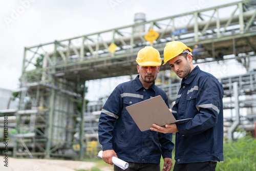 Two male petrochemical engineers with laptop working at petroleum refinery. Workers survey pipelines for oil and gas in power plant energy industry manufacturing.