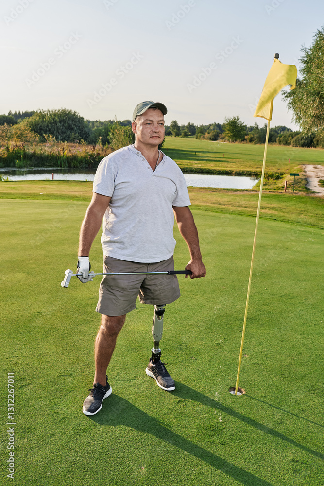 Fototapeta premium A determined golfer with a prosthetic leg stands confidently on the green, poised to make his next shot during a beautiful day