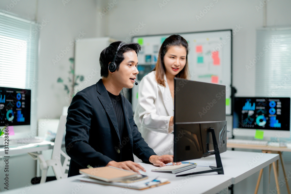 Fototapeta premium Two Asian businesspeople discussing marketing data on computer screen, working together in office