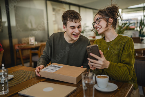 man and woman scan package card box together via mobile phone at cafe