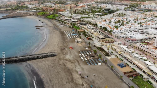 Aerial view of Costa Adeje city, Tenerife, Canary islands. Cinematic 4K footage with sandy coast, clear calm waters of Atlantic ocean, city villas, beach. Backward tracking shot, Pull-back drone video