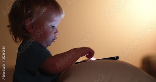 Little Child looking on mobile phone screen. Small child pressing with finger on phone touch screen. Light from the mobile phone screen illuminates the face of a small child. Cell phone and child