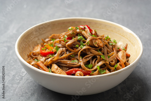 Stir fried soba noodles with chicken and vegetables in bowl on concrete background