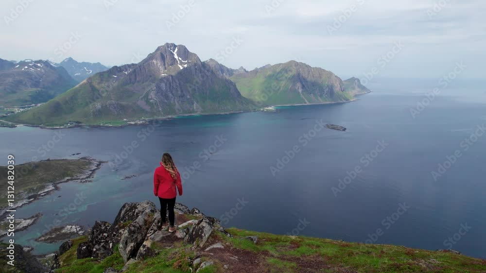 Drone Around Female Hiker in Orange Jacket in Lofoten Islands Norway. Summer Daytime at Offersoykammen Beautiful Mountains and Emerald Green Lakes. Drone Around Female Hiker in Orange Jacket in Lofoten Islands Norway. Summer Daytime at Offersoykammen Beautiful Mountains and Emerald Green Lakes.