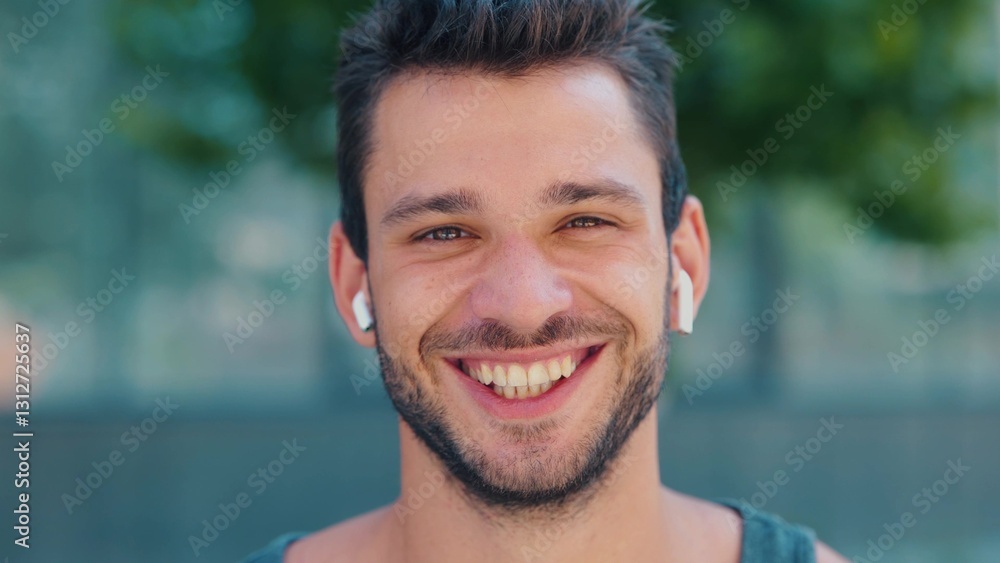 Young man exercising outside. Camera moves back from handsome positive cheerful guy smiling out loud. Listen to music through white earphones. Young man exercising outside. Camera moves back from handsome positive cheerful guy smiling out loud. Listen to music through white earphones.